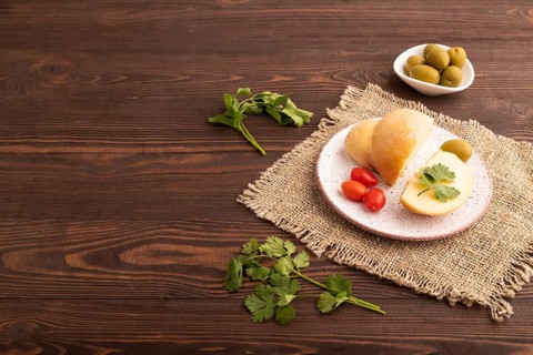 Smoked Mozzarella cheese, with tomatoes and olives on brown wooden background and linen textile,