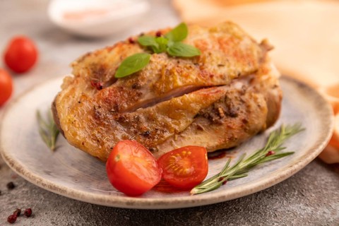 Fried Turkey Thigh with spices and rosemary on plate on brown concrete background and orange linen