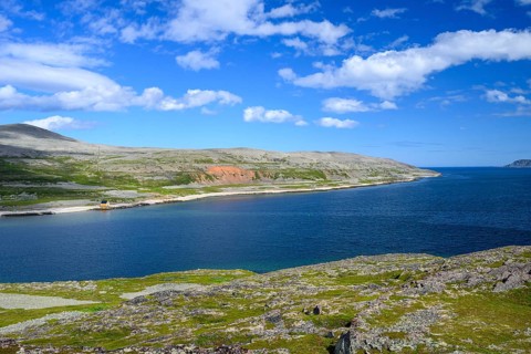Green meadows on the banks of Syltefjord with clouds in the blue sky, landscape with a lake and