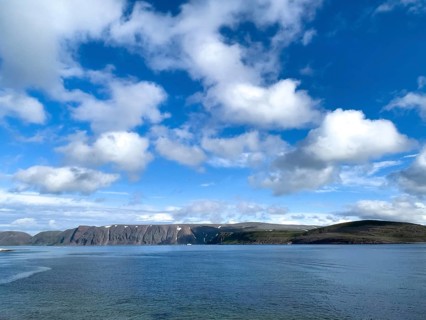 Calm sea and clear coastline under a sky with white clouds on Syltejjord on the Varanger Peninsula