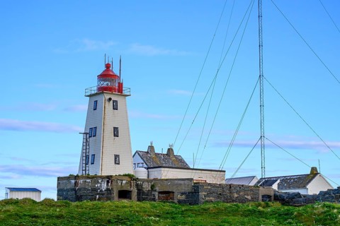White lighthouse with red tip and antennas on the bird island of Hornoya, surrounded by grassy