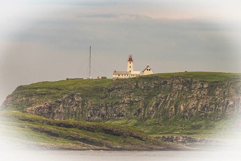 White lighthouse with red tip and antennas rises above steep rocks on the bird island of Hornoya,