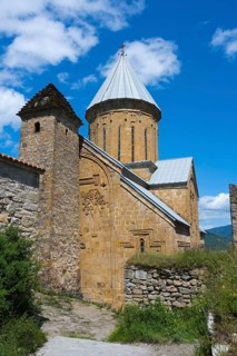 Medieval stone church with a distinctive brick tower and lush surroundings under a blue sky,