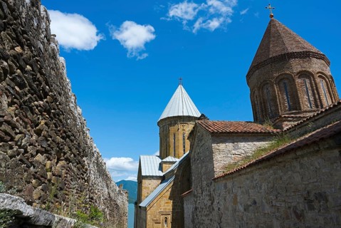 Historic monastery complex with brick towers and a surrounding stone wall under a blue sky, Ananuri