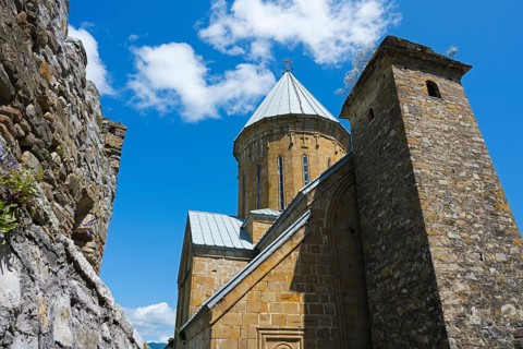 Medieval church building with a high tower and a blue sky in the background, Ananuri Castle,