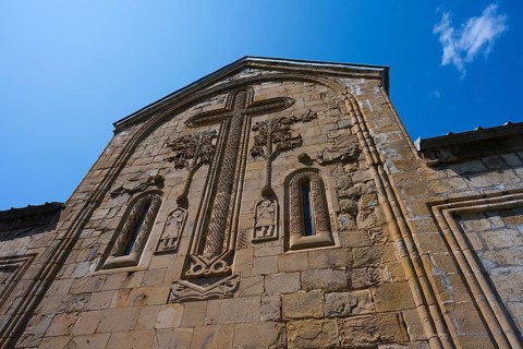 Historic church façade with large cross reliefs and decorations under a blue sky, Ananuri Castle,