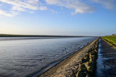 Wide view of quiet North Sea landscape with dike and water horizon, An extensive coastal landscape