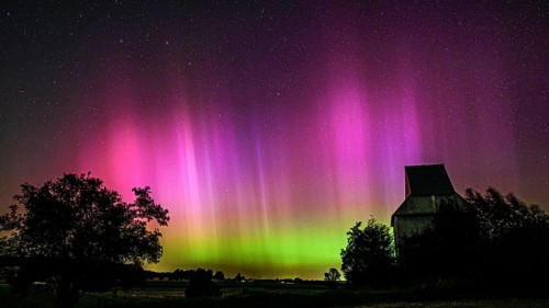 Colourful aurora above the EXPO observatory in magenta and shades of green in front of a starry