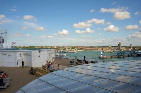 View from the ship deck of a TT-Line ferry with people and city in the background under a blue sky,
