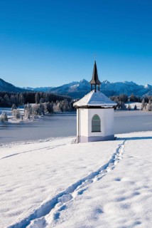 Snowy chapel against a mountain backdrop under clear blue sky with traces in the snow,