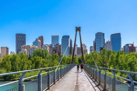 Two tourists are jogging across a pedestrian bridge in calgary, alberta with the downtown skyline