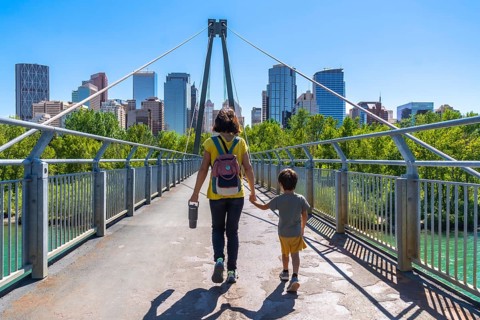 Mother and son holding hands, enjoying a sunny day walking on a bridge with the calgary city