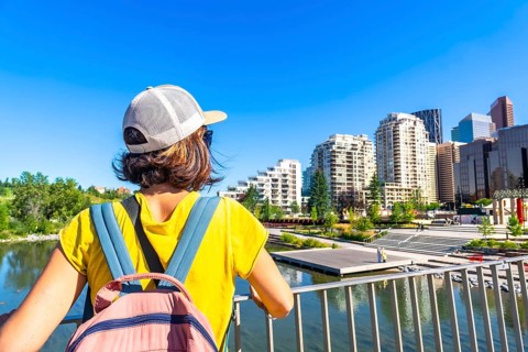 Tourist with a backpack is enjoying the cityscape of calgary, alberta, from a bridge, taking in the