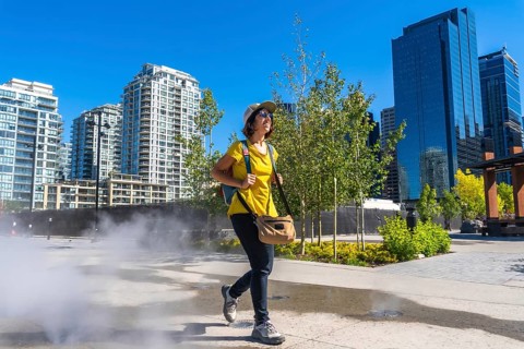 Female tourist walking through a refreshing misting station in calgary's east village, enjoying a