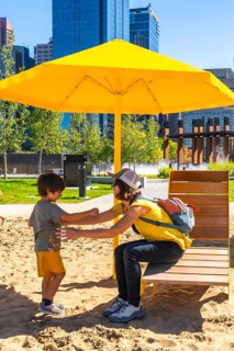 Mother and son enjoying a sunny day, playing together in a sandy urban park under a vibrant yellow