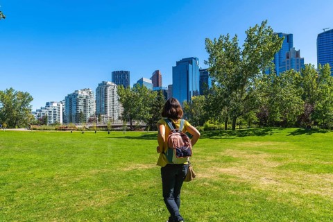 Female tourist with backpack walking on green grass in a park, enjoying the view of modern