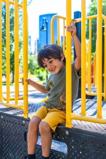 Young boy with a joyful expression sits on a playground structure, holding onto yellow bars and