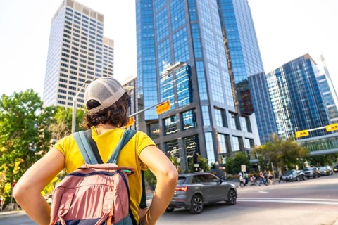 Young female tourist with backpack admiring modern skyscrapers in calgary's downtown district, a