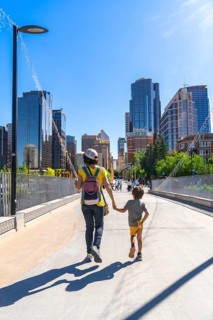 Mother and son enjoying a sunny day walking on a bridge in calgary city center, with skyscrapers