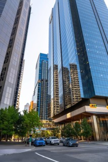 Glass skyscrapers reflecting surrounding buildings rise high above a street with cars passing by in