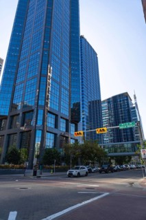Cars navigating a busy street lined with modern skyscrapers, reflecting the vibrant blue sky in