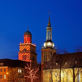 The Christmassy illuminated town hall tower and the illuminated church tower of St. John's Church