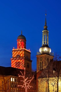 The Christmassy illuminated town hall tower and the illuminated church tower of St. John's Church