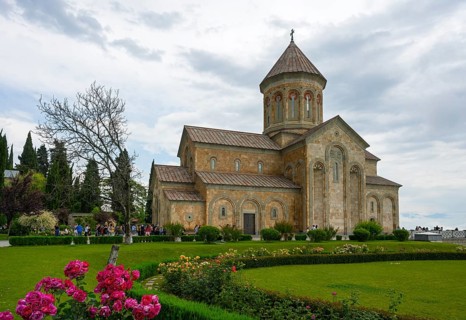 A historic church surrounded by a well-kept garden and blooming flowers under cloudy sky, Bodbe