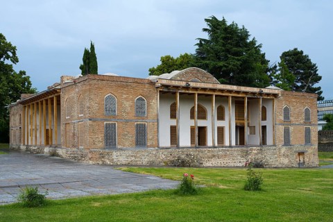 Old building with impressive brick walls and elegant columned entrance in garden surroundings,