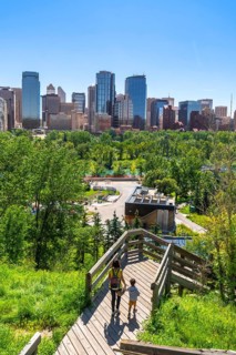 Mother and son walking down wooden stairs in a park, enjoying the view of the calgary skyline on a