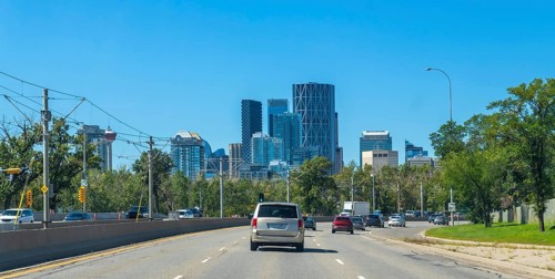 Vehicles are driving on a highway with the calgary skyline, featuring modern skyscrapers and lush