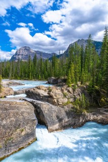 Turquoise water flows under natural bridge rock formation on bow river with evergreen trees,