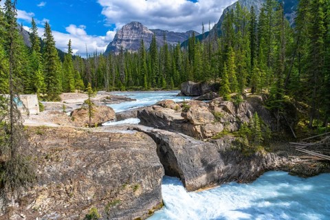 Turquoise bow river flowing beneath a natural bridge rock formation, framed by cascade mountain,