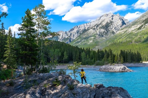 Tourist standing on rocks by the turquoise waters of lake minnewanka, admiring the breathtaking