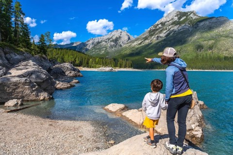 Mother points across the turquoise expanse of lake minnewanka, sharing a moment of awe with her son