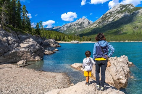 Mother and son standing on a rock, admiring the stunning turquoise waters of lake minnewanka,