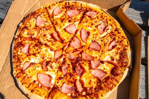 Sliced pizza with ham and melted cheese inside a cardboard box is waiting to be eaten outdoors,