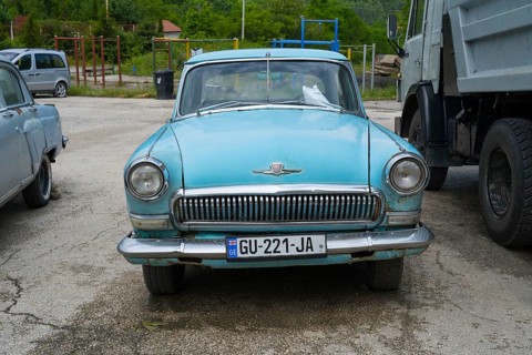 A blue classic car is parked in a parking lot next to a truck, GAZ M-21 Volga, Georgia