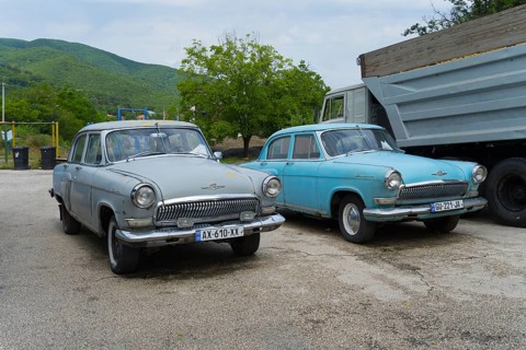 Two vintage cars are parked in a parking lot in front of a hilly landscape, GAZ M-21 Volga, Georgia