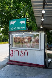 A small stand with meat presentation and signs, surrounded by green trees, butcher, small, mobile