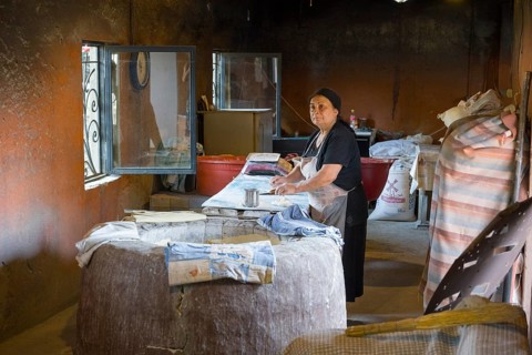 An elderly woman works in a traditional, rustic bakery with bread and baking supplies, bakery,