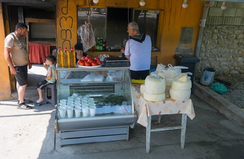 Market stall with cheese and tomatoes surrounded by a few people in an urban environment selling