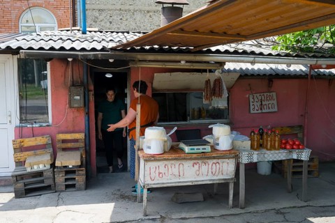 A rustic market stall with handmade products and people talking, selling cheese and tomatoes and
