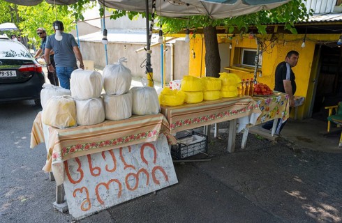 Market stand with various types of cheese and products under trees at a busy market selling cheese,