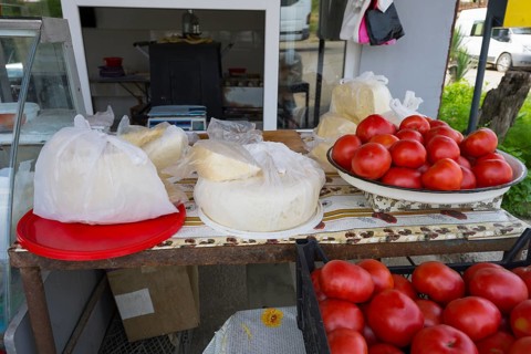 A market stall with tomatoes and cheese, fresh and on plates and wrapped in plastic, selling cheese