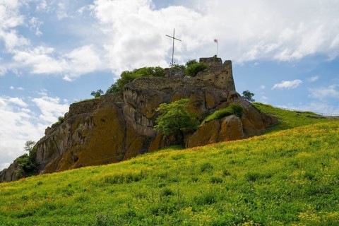 An old castle on a green hill under cloudy sky with a cross on top, Kveshi fortress, Bolnisi,