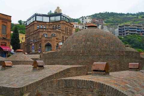 Historic brick buildings and urban baths in front of green hills, sulfur baths, Abanotubani spa