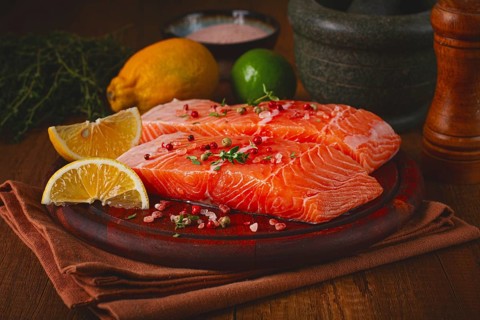 Two salmon fillets rest on a wooden platter. The fillets are garnished with herbs and spices. Lemon