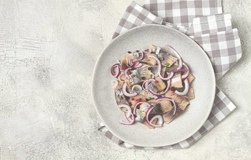 Salted herring, with spices and red onion, sliced fillet, on a plate, top view