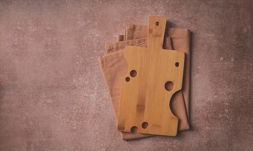Wooden cutting board, rectangular with handle, cheese shape with holes, on a kitchen towel, top